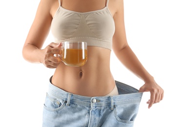 Young woman in old big jeans with cup of tea showing her diet results on white background, closeup