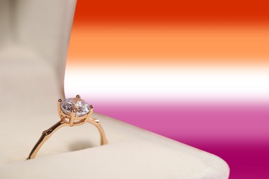 Box with beautiful engagement ring on background in color of lesbian flag, closeup