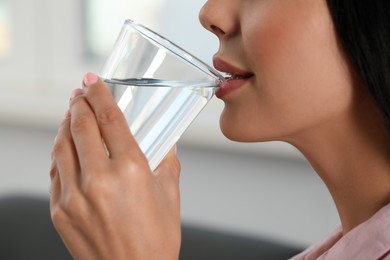 Young woman drinking water indoors, closeup. Refreshing drink