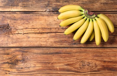Bunch of ripe baby bananas on wooden table, top view. Space for text