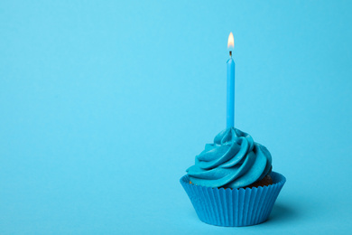 Delicious birthday cupcake with burning candle on light blue background. Space for text