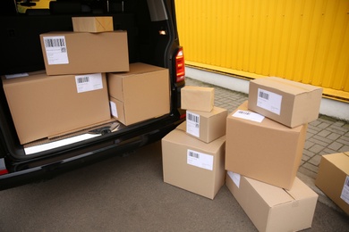 Black delivery van and many different parcels near yellow building outdoors. Courier service