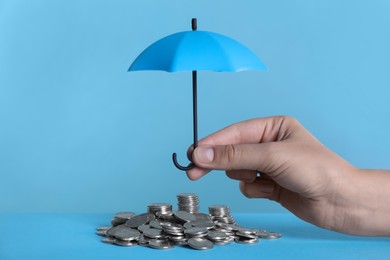 Woman holding small umbrella over coins on light blue background, closeup