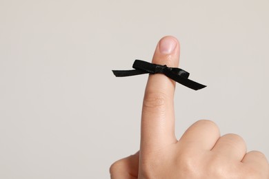 Man showing index finger with black tied bow as reminder on white background, closeup. Space for text