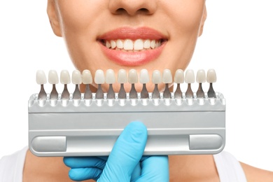 Doctor checking young woman's teeth color on white background, closeup. Cosmetic dentistry