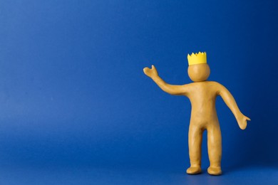 Plasticine figure with crown on head against blue background. Space for text