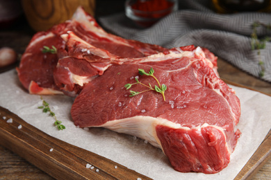 Fresh raw beef cut with thyme and salt on wooden table, closeup
