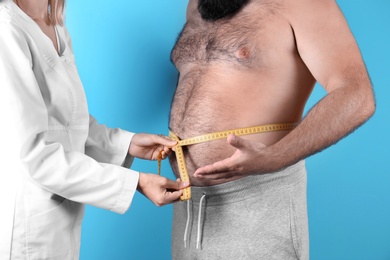 Doctor measuring fat man's waist on color background. Weight loss