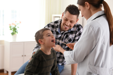 Father and son visiting pediatrician. Doctor examining little patient's throat in hospital