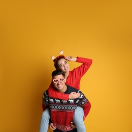 Couple in Christmas sweaters, Santa headband and party glasses on yellow background