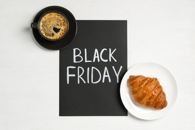 Cup of coffee, croissant and sheet of paper with words Black Friday on white background, flat lay