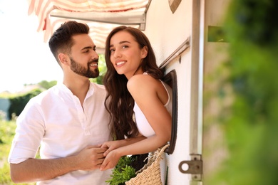 Happy young woman leaning out of trailer window to hug her boyfriend. Camping vacation