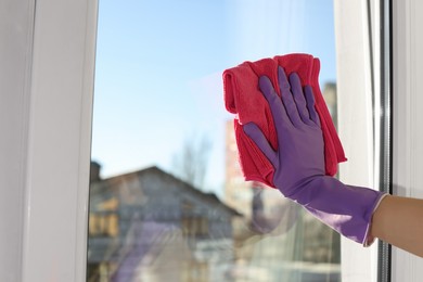 Young woman cleaning window glass with rag at home, closeup. Space for text