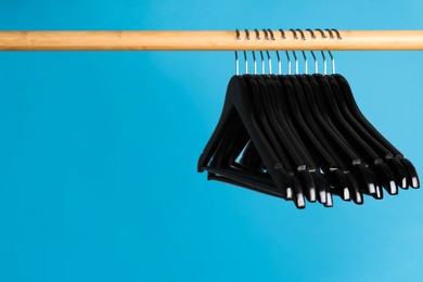 Photo of Black clothes hangers on wooden rail against light blue background. Space for text