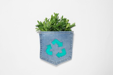 Photo of Twigs of green plant in jeans pocket with recycling symbol on white background, top view
