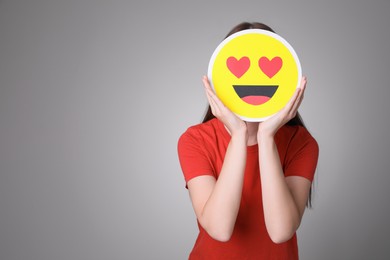 Photo of Woman covering face with heart eyes emoji on grey background, space for text