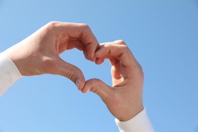 Man showing heart against blue sky outdoors on sunny day, closeup of hands