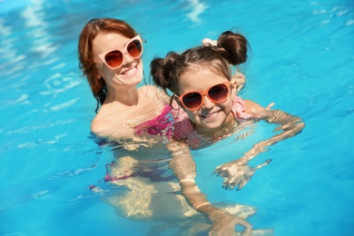 Young woman teaching her daughter to swim in pool