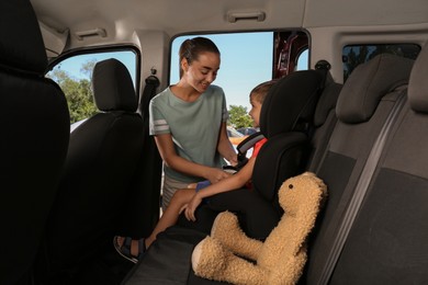 Mother fastening her son with car safety belt in child seat