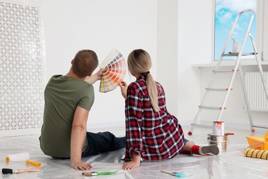 Photo of Couple with paint chips discussing new wall color in apartment during repair, back view