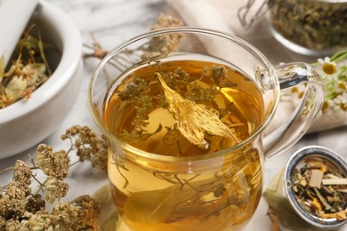 Freshly brewed tea and dried herbs on white marble table, closeup