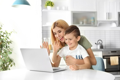 Photo of Mother and her son using video chat on laptop at table in kitchen