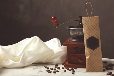 Scented sachet, coffee grinder and beans on white marble table against black background, space for text