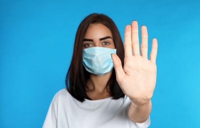 Young woman in protective mask showing stop gesture on light blue background. Prevent spreading of coronavirus