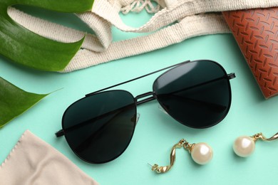 Photo of Stylish elegant sunglasses with brown leather case and earrings on turquoise background, flat lay