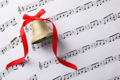 Photo of Golden bell with red bow on music sheets, top view. Christmas decor