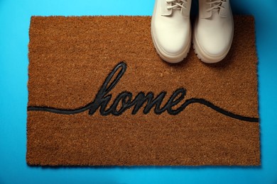 Photo of Doormat with word Home and stylish boots on light blue background, flat lay