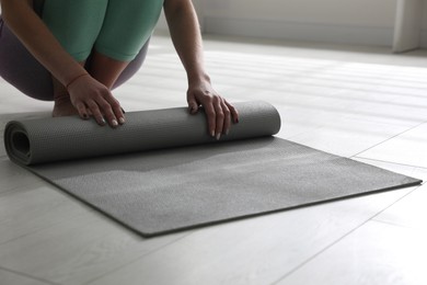 Photo of Woman rolling her mat on floor in yoga studio, closeup
