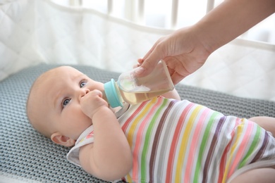 Lovely mother giving her baby drink from bottle in cot