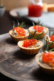 Photo of Delicious tartlets with red caviar and cream cheese served on wooden board, closeup