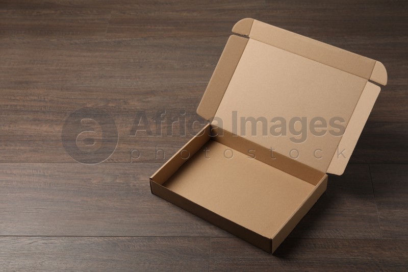 Empty open cardboard box on wooden table. Space for text
