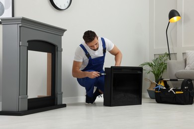 Professional technician with screwdriver installing electric fireplace in room