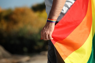 Man with rainbow LGBT flag as gay symbol outdoors, closeup. Space for text