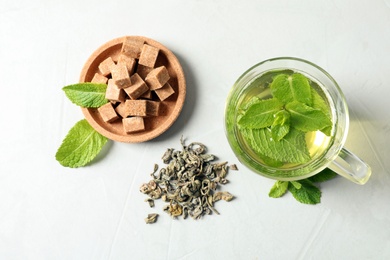 Cup with hot aromatic mint tea, dry leaves and sugar cubes on table, top view