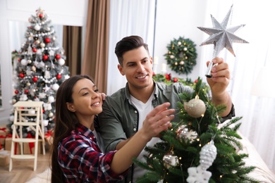 Photo of Couple decorating Christmas tree with star topper in room