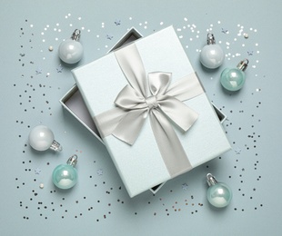Photo of Beautiful gift box, Christmas balls and confetti on grey background, flat lay