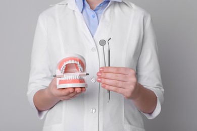 Dentist holding jaws model and tools on light grey background, closeup
