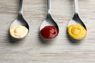 Spoons with mustard, ketchup and mayonnaise on wooden table