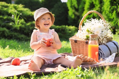 Cute little baby girl with nectarine on picnic blanket in garden