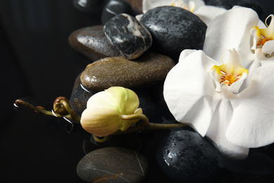 Photo of Spa stones and orchid flowers in water on black background, closeup. Zen lifestyle