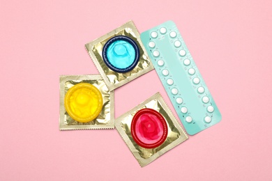 Condoms and birth control pills on pink background, top view. Safe sex