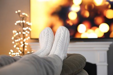Woman wearing knitted socks in room decorated for Christmas, closeup