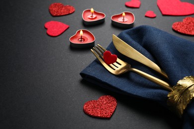 Photo of Cutlery set, burning candles and decorative hearts on black background, space for text. Romantic table setting