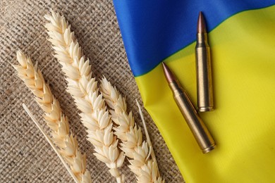 Photo of Bullets, spikelets and national Ukrainian flag on burlap, flat lay