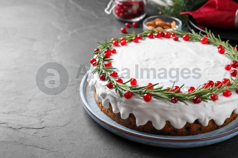 Photo of Traditional Christmas cake decorated with rosemary and cranberries on dark grey table, space for text