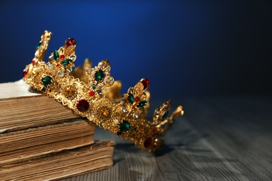 Beautiful golden crown and old books on wooden table. Fantasy item